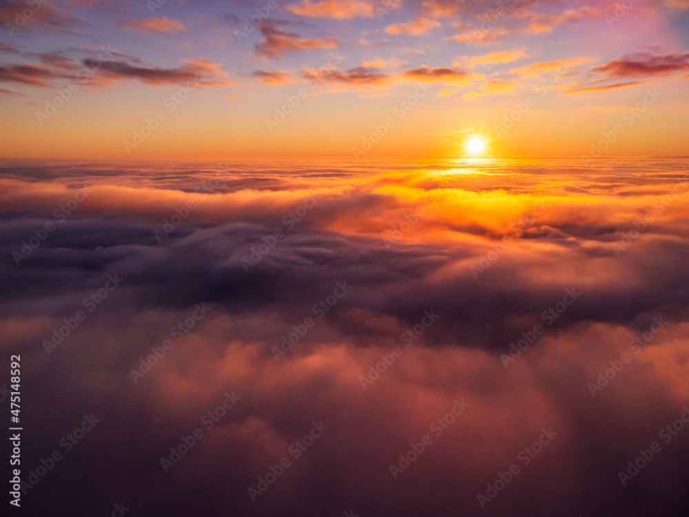 Poster Dream-like photo of clouds of mist and a setting sun in the background. Flying with a drone above thick fog at sunset