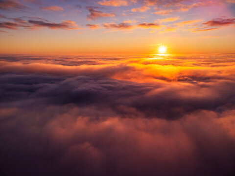 Dream-like photo of clouds of mist and a setting sun in the background. Flying with a drone above thick fog at sunset