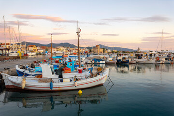 Fototapeta na wymiar Colorful fishing boats line the harbor of the Greek island of Aegina, Greece at dusk, with the waterfront promenade and shops in view.