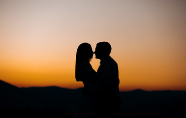 Fototapeta na wymiar Groom and bride stand on the mountain against the background of sunset