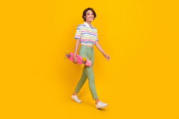 Full body profile side photo of young attractive girl good mood go skateboard sporty isolated over yellow color background