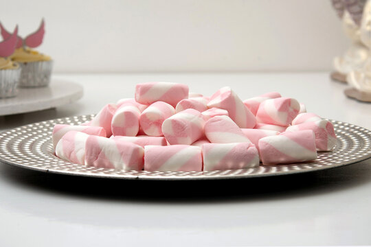 Plate full of mini white and pink marshmallows on a white background.