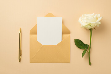 Top view photo of ordered composition open pastel yellow envelope with card golden pen and white rose on isolated beige background with empty space