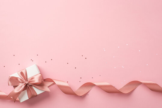 Top View Photo Of St Valentine's Day Decorations White Gift Box With Bow Pink Curly Ribbon And Sequins On Isolated Pastel Pink Background With Copyspace