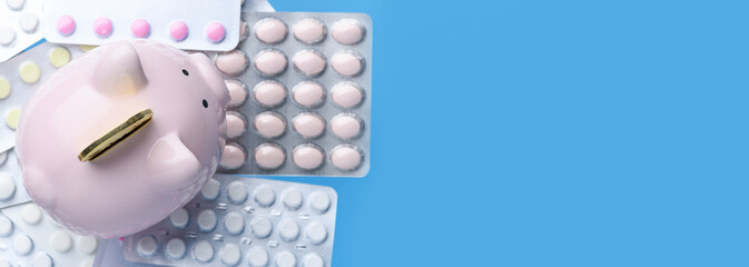 Pink piggy Bank with coin and pills in a blister pack on blue background, view from above. Coronavirus, 2019-nCoV. Banner.