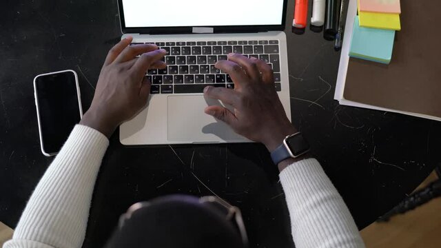 Top view of dark skinned student typing article ext on laptop keyboard and sitting at the desk. View from above,  male freelancer working on project using netbook computer. Browsing and researching