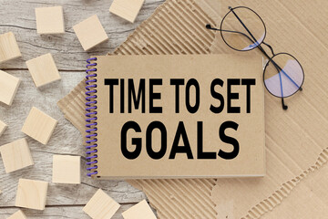 time to set goalos. text on a notebook that lies on a working wooden table near wooden blocks on torn paper