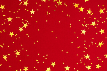 Gold stars on red background. Festive red background with gold stars confetti. Flat lay, top view,...
