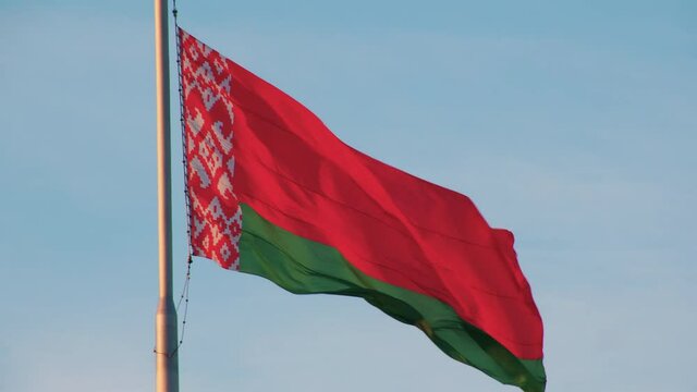 CLOSE-UP: Single red-green flag of the Republic of Belarus waving in the wind against a blue sky. Concept of a totalitarian state with a dictator at its head. Violation of basic human rights.
