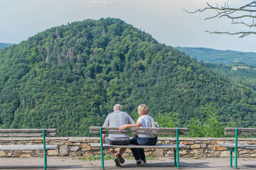 Fototapeta na wymiar Älteres Paar auf der Ruhebank mit Blick auf bewaldeten Hügel