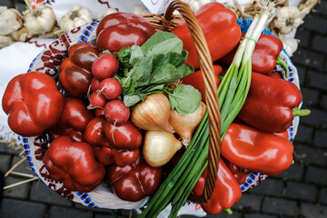 Shallow depth of field (selective focus) image with a basket filled with organic fresh vegetables (red pepper, radish, spring onion, tomatos) for sale in an outdoors market in Bucharest, Romania.