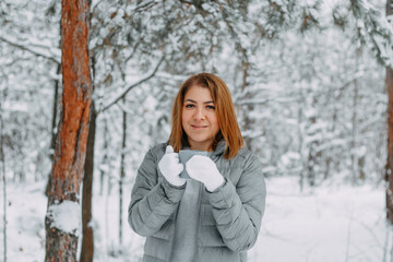 Fototapeta na wymiar A cute girl with short hair in a gray jacket and knitted white mittens is drinking hot tea in a snowy forest. Cozy and warm in the winter season.selective focus