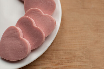 sausage cut in the form of hearts on a white plate on a wooden background with a place for text