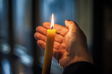 Hands closeup of religious man holding lit candle and praying