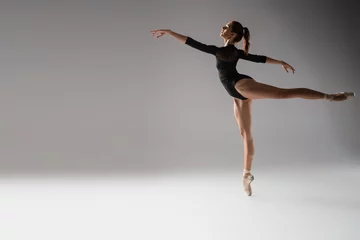 Rollo full length of woman in ballet shoes dancing with outstretched hands on dark grey © LIGHTFIELD STUDIOS