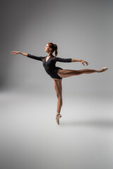 full length of pretty woman in ballet shoes performing ballet dance while standing on pointe shoe on dark grey