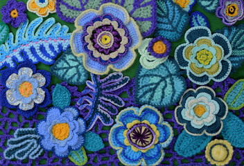 A decorative arrangement of handmade flowers and leaves on a  crochet background.