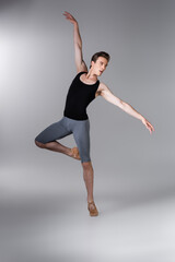 Fototapeta na wymiar young and graceful man gesturing while performing ballet dance on dark grey