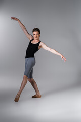 Fototapeta na wymiar young and graceful ballet dancer gesturing while performing ballet dance on dark grey