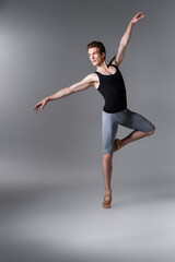 Fototapeta na wymiar young dancer in tank top gesturing while performing ballet dance on dark grey