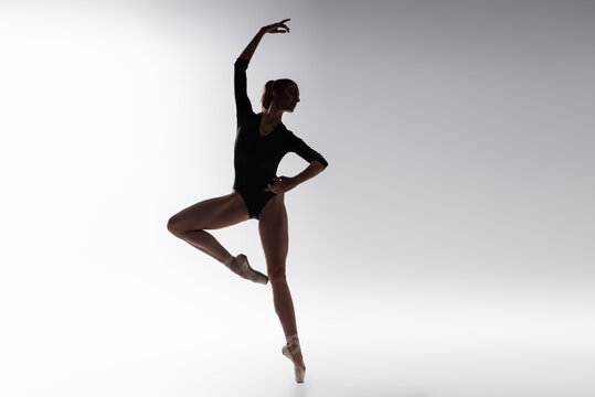 silhouette of ballerina in bodysuit dancing on gray