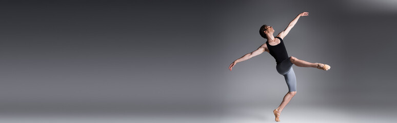 full length of elegant man performing ballet dance on dark grey, banner