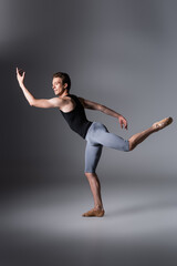 full length of graceful ballet dancer in tank top gesturing on dark grey