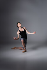 full length of elegant ballet dancer standing on knee while performing ballet dance on dark grey