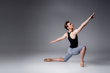 full length of young ballet dancer in tank top performing dance on dark grey