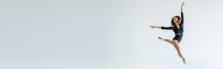 full length of ballerina in black bodysuit jumping isolated on grey, banner