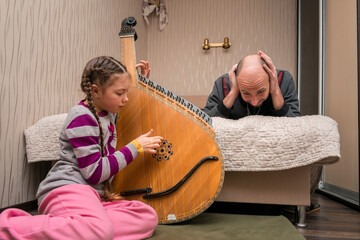 The child loudly plays the bandura, and dad lies on the bed with his hands over his ears. A girl...