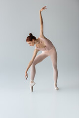 full length of ballerina in ballet shoes dancing with outstretched hand on grey
