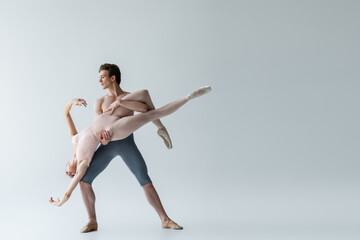 full length of shirtless man and sensual ballerina performing ballet dance on grey