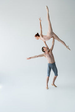 Fototapeta full length of shirtless ballet dancer lifting graceful ballerina in bodysuit on gray