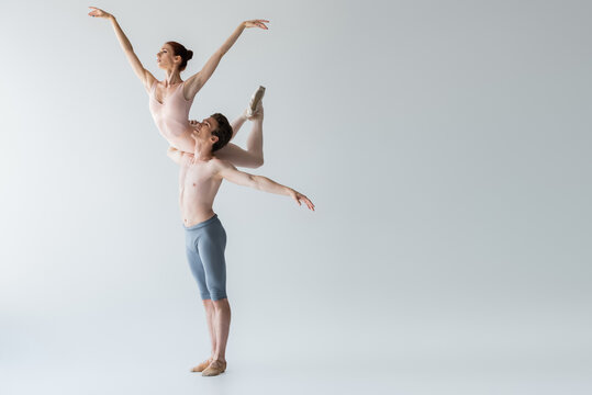 full length of shirtless ballet dancer lifting ballerina isolated on grey