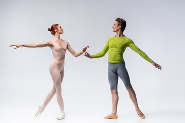 Obraz na płótnie Canvas full length of young ballet dancer looking at graceful ballerina on grey