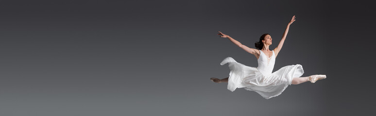 Fototapeta full length of graceful woman in white dress jumping isolated on grey, banner obraz
