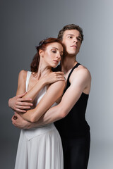 man hugging graceful ballerina in white dress on dark grey