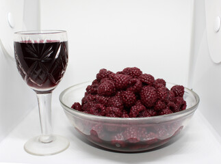 a glass of red wine is on the table with a vase of fresh raspberries for a healthy and vitamin dinner