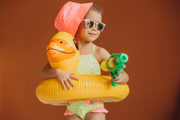 Baby girl isolated wearing swimsuit and rubber duck tube and holding water pistol