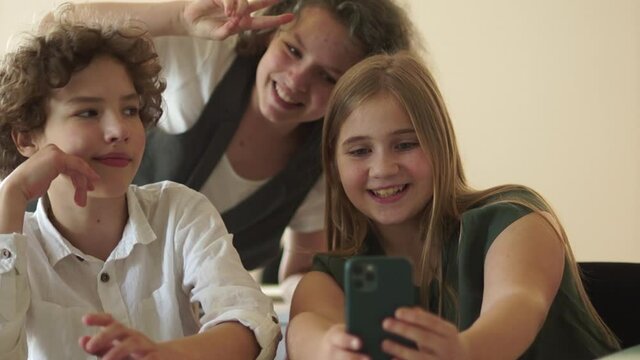 Girl taking a selfie. Teenagers are photographed, a portrait of a boy and two girls at a desk with smartphone