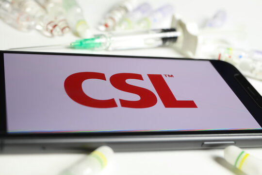 Viersen, Germany - December 1. 2021: Closeup of mobile phone screen with logo lettering of CSL Behring, serum vials and syringe background (selective focus on center of letter S)