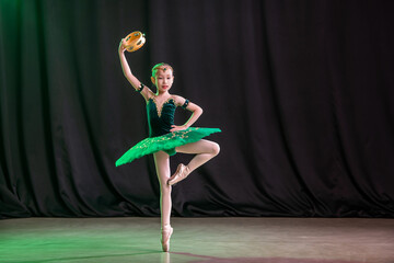 A little girl ballerina is dancing on stage in a tutu on pointe shoes with a tambourine, a classic...