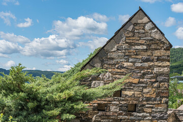 Steinernes Haus mit Steildach vor blauem Himmel mit Wolken