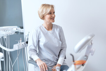 Cheerful stomatologist looking away when sitting in her cabinet