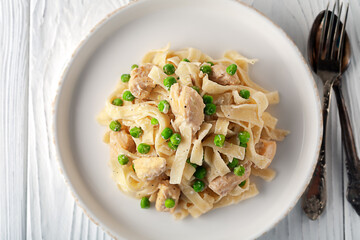 Homemade pasta with green peas, chicken and cream sauce on a white wooden background on a white wooden background