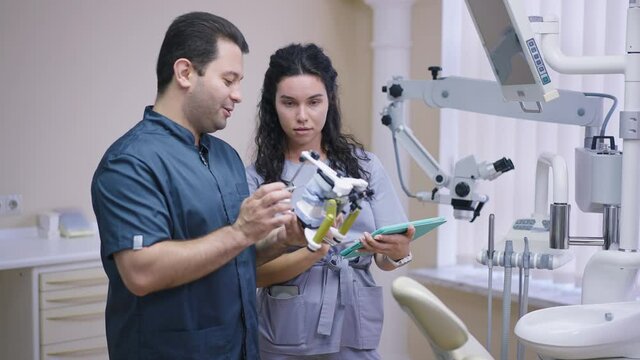 Positive expert Middle Eastern male dentist talking pointing at dental sample model in slow motion. Concentrated female Caucasian student listening learning dentistry with practitioner orthodontist
