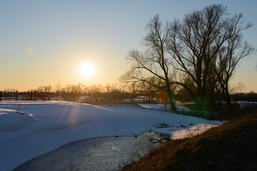 Spring evening landscape with a ravine with frozen water and snow drifts