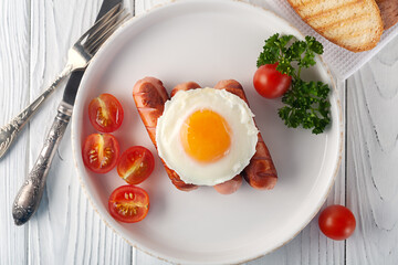 Scrambled eggs with sausages, tomatoes and toasts on a white wooden background