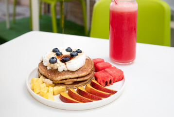 Blueberry pancakes with fresh fruit, peaches, pineapple, watermelon. In the background a delicious red orange juice.